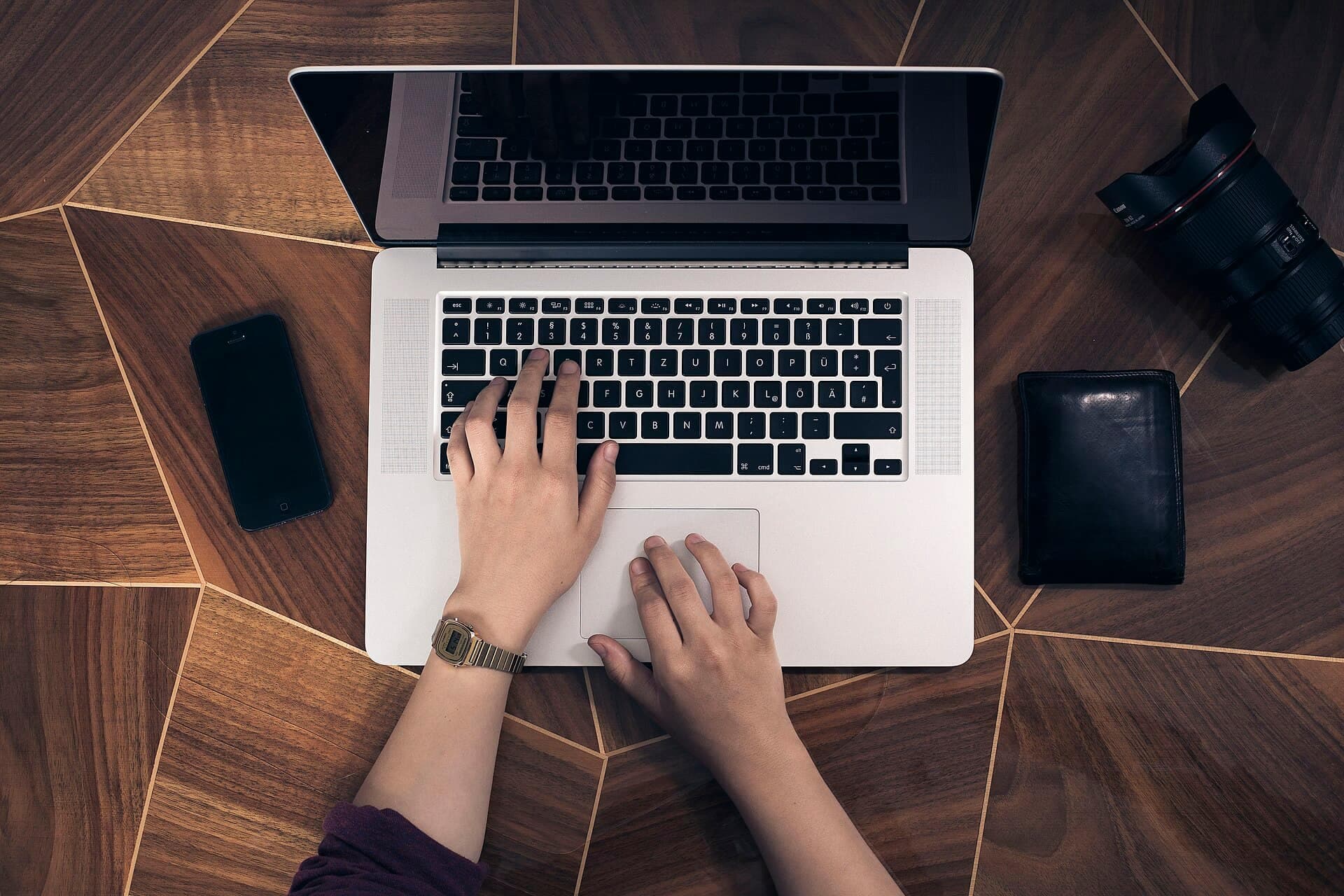 Hands typing on a laptop keyboard, seen from above, on a wooden desk.