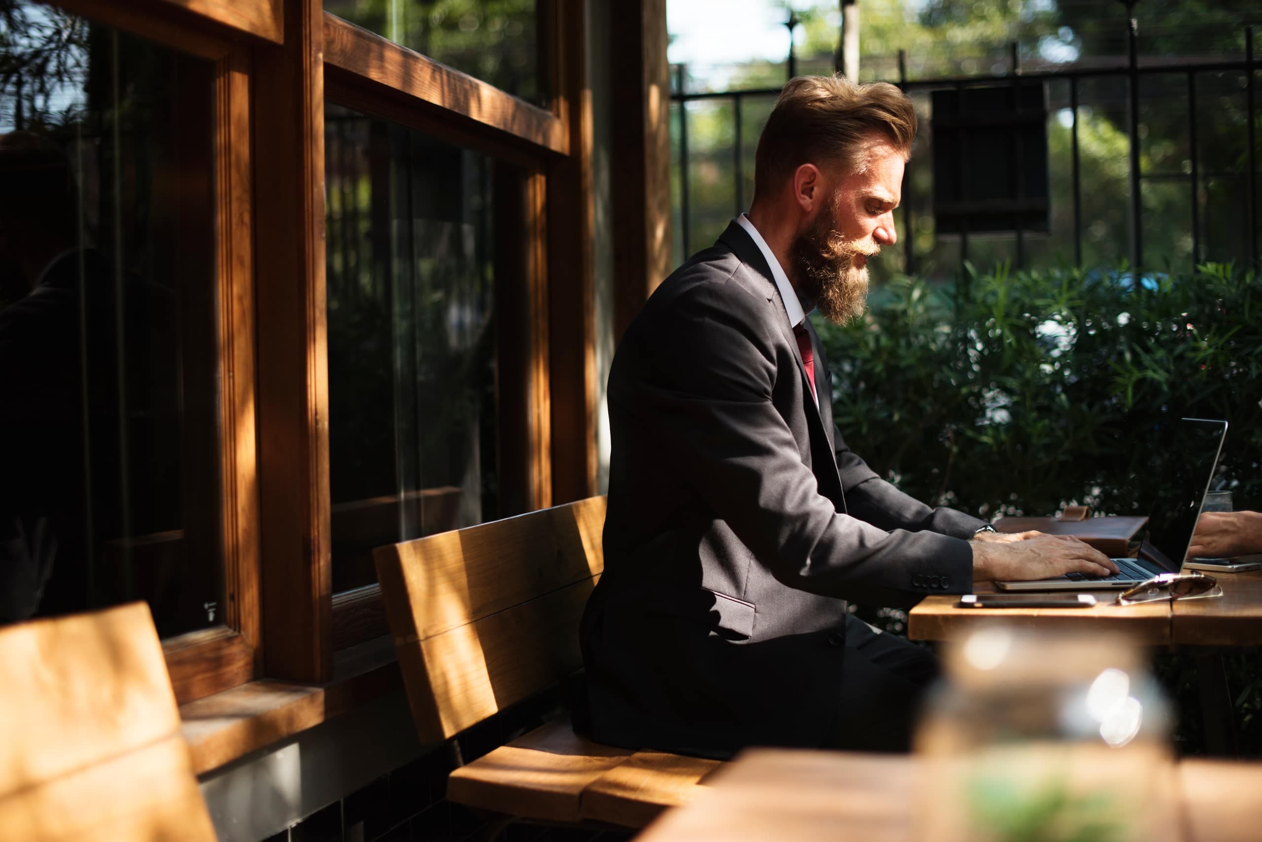 A person in a suit working on a laptop at an outdoor table in low evening light.